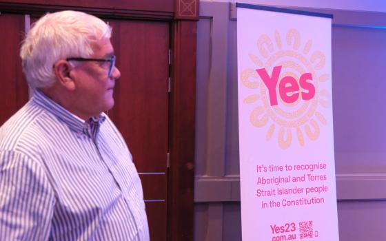 Mick Gooda standing beside a Yes campaign banner